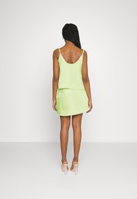 Vestido de cetim verde claro com um corte solto, apresentando alças finas, costas em formato de mergulho e uma bainha que sobe ligeiramente nas laterais.