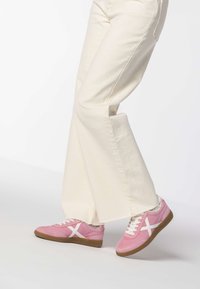 Baskets roses à lacets avec des accents blancs, présentant un dessus texturé et une semelle en caoutchouc marron. Portées avec un pantalon large crème.