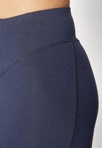 Mörkblå högmidjade leggings med en slät yta, som har en diagonal sömdetalj och förstärkt sömnad längs kanterna.