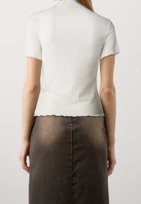 Biały prążkowany top z krótkim rękawem i falowanym dołem, zestawiony z ciemnobrązową spódnicą z denimu z centralnym szwem i zamkiem błyskawicznym.