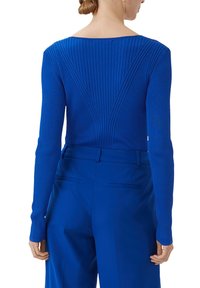 Niebieski prążkowany top z długim rękawem i szerokim dekoltem oraz geometrycznym wzorem z tyłu, w połączeniu z dopasowanymi spodniami o wysokim stanie. Gładka tekstura.