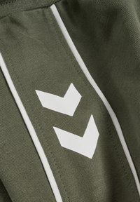 Olivengrøn atletisk stof med en glat tekstur, der har to hvide chevrondesigns og hvide sidelister. Enkel og moderne udseende.