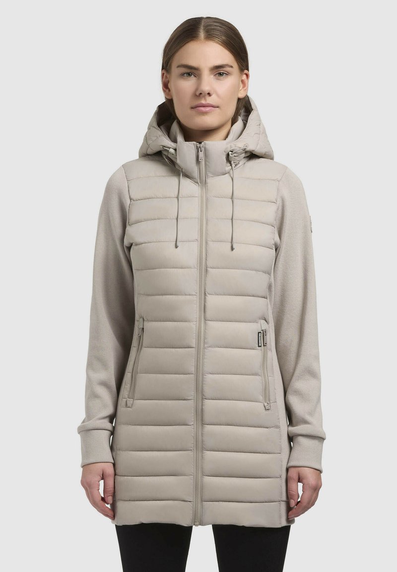 Beige hybridjakke med en fyldig quiltet krop og bløde stofærmer, med hætte, fuld lynlås og to sidelommer.