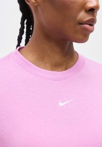 Κοντινό πλάνο ενός ατόμου που φοράει ανοιχτό μωβ μπλουζάκι Nike με λευκό λογότυπο σφύρας εμφανές κοντά στον γιακά.