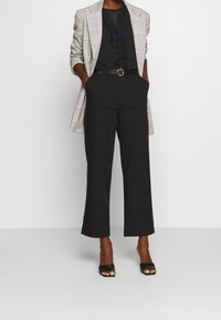 Šedý kostkovaný blazer, černý ruffled top, černé široké kalhoty a černé otevřené lodičky. Má páskový pas a hladké textury.