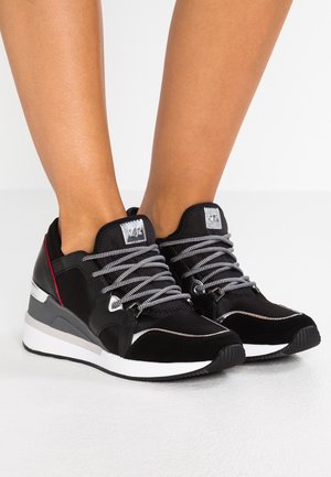 Scarpe da ginnastica nere con una combinazione di materiali in pelle scamosciata e mesh. Presentano accenti argentati, lacci grigi spessi e una suola intermedia bianca.