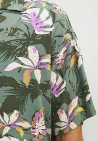 Kurzarmhemd aus grünem Stoff mit einem floralen Muster, das rosa und weiße Blumen sowie dunkelgrüne Blätter zeigt, und einem lässigen Schnitt.