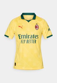 Gul AC Milan fotbaltrøye med grønn krage og ermekanter, rød Puma-logo, og Emirates Fly Better sponsor tekst på forsiden.