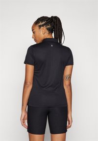 Črn športni polo s kratkimi rokavi, teksturirana tkanina in majhna oznaka pri vratu. V kombinaciji s črnimi kratkimi hlačami.