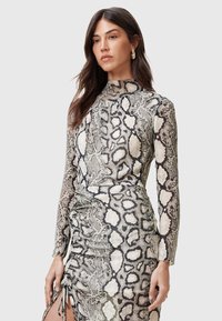Abito a maniche lunghe con stampa serpente in tonalità neutre e collo alto. Design drappeggiato con arricciature laterali e uno spacco alto fino alla coscia. Texture liscia.