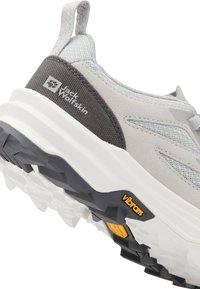 Helle graue Sneaker aus Wildleder und Mesh-Material, mit einer schwarzen strukturierten Ferse, einer weißen Sohle und gelbem Vibram-Branding auf der Sohle.