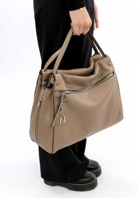 Tan leather handbag with a slouchy design, featuring silver hardware, zippered pockets, and a charm detail. Handles for carrying.