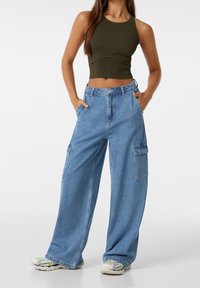 Ljusblå vida cargofickbyxor med flera fickor, i kombination med en figurnära olivgrön ribbad crop top. Materialet verkar vara en bomullsblandning.