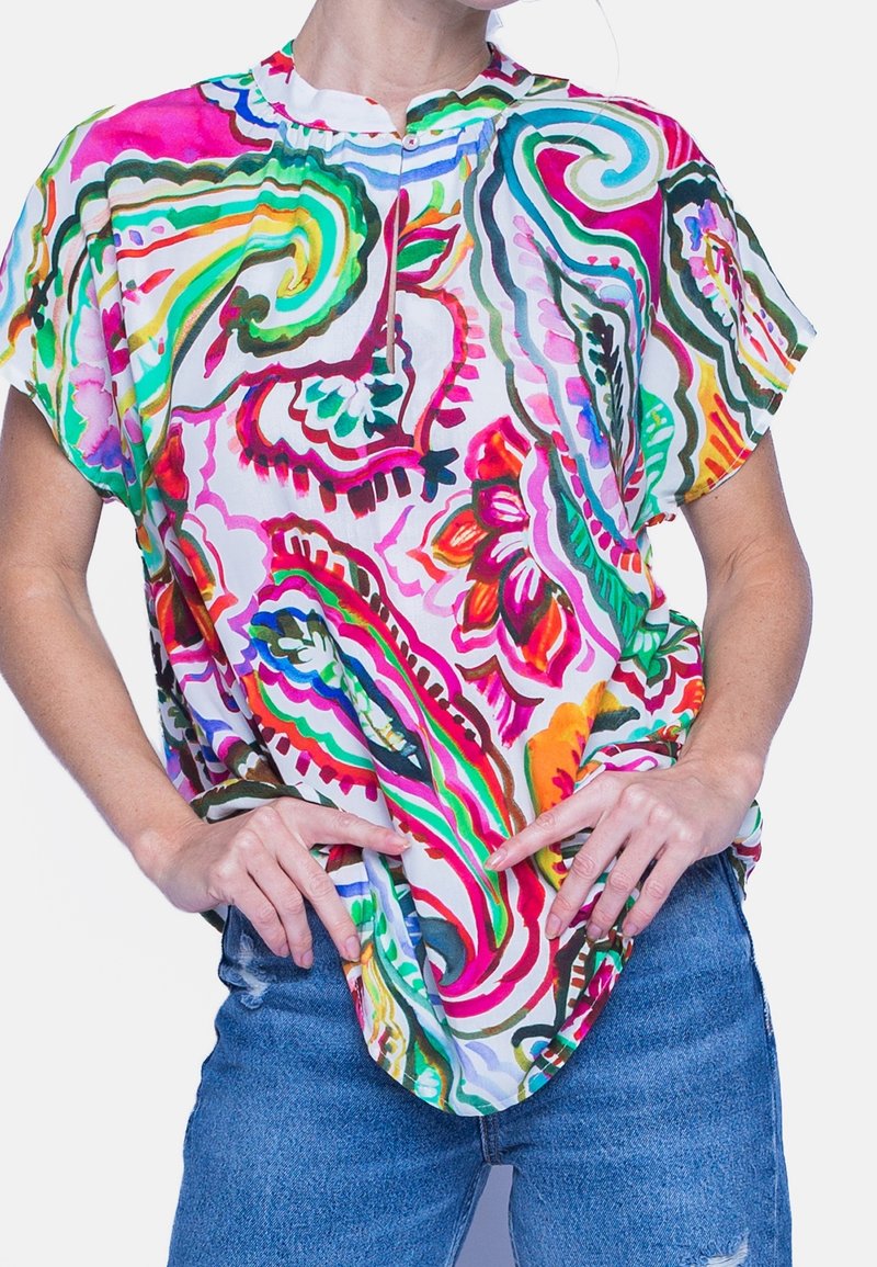 Värikäs, lyhythihainen paita, jossa on valkoinen tausta ja eloisat kukka- ja paisley-kuviot vaaleanpunaisena, vihreänä ja oranssina; pehmeä kangas, rento istuvuus.