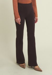 Pantalones acampanados negros de talle alto con cinturilla texturizada, tejido suave y detalles de costura. Combinados con elegantes tacones puntiagudos beiges brillantes.