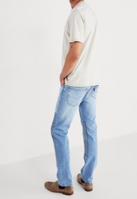 Kortärmad beige randig skjorta med blå jeans och bruna mockastövlar. Skjortan har en rund nacke; jeansen har distinkta sidpaneler.