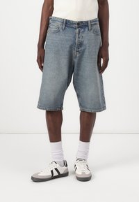 Denim shorts in light blue, featuring a relaxed fit, frayed hem, front pockets, and belt loops, paired with white socks and sneakers.