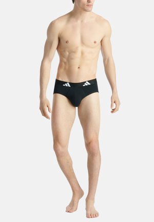 Schwarze Schwimmshorts mit weißem Markenlogo am Bund, enganliegendes Design, elastisches Material, tief geschnittene Leibhöhe und minimale Rückendeckung.