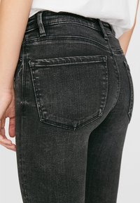 Černé džíny z denimu s naobleným střihem, obsahující dvě zadní kapsy, jemné vyblednutí a vysoký pas. Materiál má hladkou strukturu.