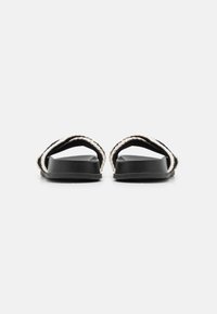 Svarte flate sandaler med to vevde stropper som har en kremfarget aksent. Sålen er glatt og litt buet, noe som gir et uformelt design.