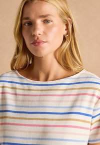 T-shirt with a wide neckline made of soft fabric, featuring horizontal stripes in pink, blue, and tan. Smooth texture, short sleeves.
