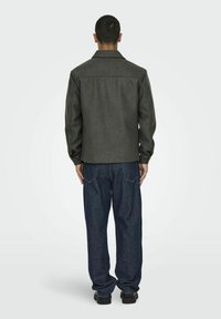 Grijze wolmix jas met een rechte snit, zichtbare stiksels en een kraag. Gecombineerd met ruime donkerblauwe spijkerbroeken en zwarte schoenen.