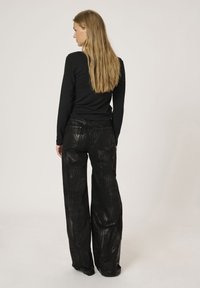 Zwart lang mouwtop gecombineerd met zwarte brede broek met een glanzend, textuur patroon. Stof lijkt soepel met zichtbare zaknaad.