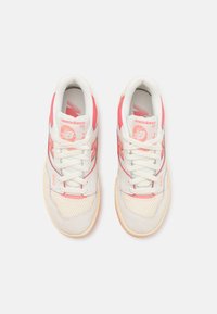 New Balance 550 tenisice imaju bijeli kožni gornji dio s koraljnim akcentima, mrežastim dijelovima i podstavljenim jezikom, uparenim s bež gumiranim potplatom.