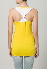 Top sin mangas amarillo con un diseño de tirantes cruzados en blanco; cuenta con el logo "Bench." en amarillo en la parte superior de la espalda. Textura de tela suave.