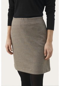 Brun rutiga kjolen med en figurnära design, tillverkad av ett texturerat tyg, knälång, matchad med en svart långärmad tröja och enfärgade svarta strumpbyxor.