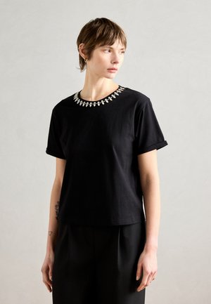 Black cotton t-shirt with rolled short sleeves and a decorative beaded neckline. Smooth texture, simple design, and relaxed fit.