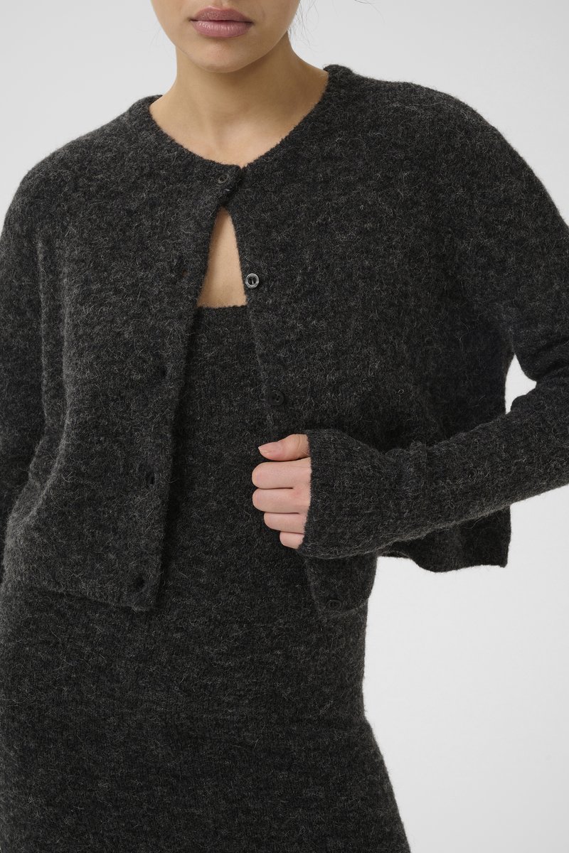 Mørkegrå cropped cardigan i blød, tekstureret uld. Har knaplukning og lange ærmer med tommelfingerhuller, som er parret med en matchende kjole.