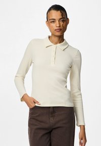 Rebrasto kremno dolgo-sleeve polo majica z gumbnim zapenjanjem in klasičnim ovratnikom. Tkanina se zdi lahka z gladko teksturo.