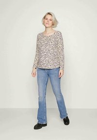 Camisola de manga longa em bege com um padrão de leopardo preto, combinada com jeans claros de corte flare e sapatos pretos. Textura suave, ajuste descontraído.