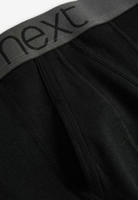 Boxeri negri din bumbac, cu o curea elastică moale de culoare gri, având cuvântul "next" scris cu litere negre, prezentând o textură fină și detalii de cusătură.