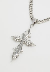 Silberfarbene Halskette mit einem genagelten Kreuzanhänger, polierter Oberfläche und einem klobigen Kettendesign. Der Anhänger hängt an einem Karabinerverschluss.