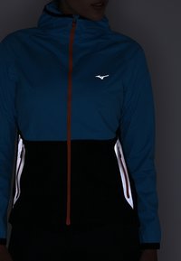 Lightweight, blue and black jacket with an orange zipper. Features reflective accents and a zippered pocket. Hooded design.