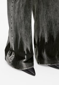 Wide-legged jeans in faded black denim with a shiny texture, paired with pointed black high-heeled shoes, featuring sleek contours.