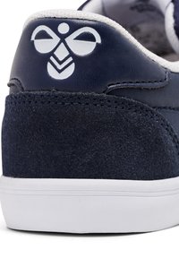 Marineblauwe sneaker van suède en leren materialen. Bevat een wit logo en stiksels op de hiel, een rubberen zool en een gestructureerde bovenkant.