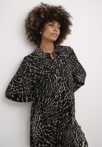 Camicia a stampa leopardata nera e beige con colletto, maniche ampie e frontale con bottoni. Tessuto morbido, dettaglio con motivo testurizzato.