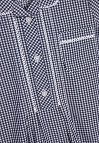 Koszula w granatowo-białą kratkę z zapięciem na guziki, białymi falbaniastymi wykończeniami przy kołnierzy oraz kieszenią na piersi.