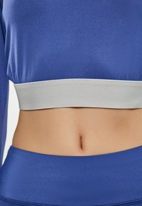 Blauwe fitted top met een brede lichtgrijze elastische band aan de onderkant, gladde textuur en korte mouwen, met een gestroomlijnd ontwerp.