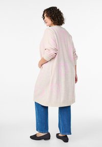 Garšs, bēšs kardigāns ar rozā sirds rakstiem, ribotām piedurknēm un mīkstu tekstūru. Saskaņots ar ziliem platām kājām džinsiem un melniem dzīvokļiem.