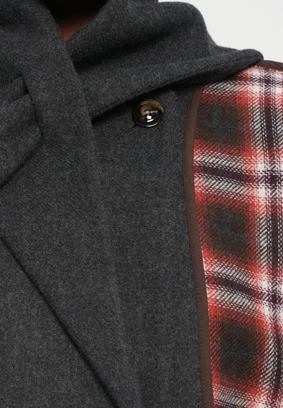 Donkergrijze wollen jas met een grote kraag, zwarte knopen en een zijpaneel met een rood-witte ruitpatroon, omrand met bruin.