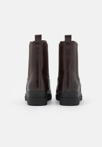 Bottes à cheville en cuir marron foncé avec une finition lisse, dotées de panneaux élastiques latéraux, d'une languette de tirage et d'une semelle en caoutchouc noire texturée.