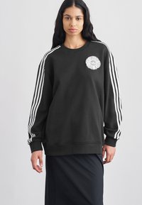 Μαύρο φούτερ από βαμβακερό μείγμα, με λευκό σχέδιο με τρεις ρίγες στα μανίκια και υφασμένο λογότυπο λουλουδιού στο στήθος.