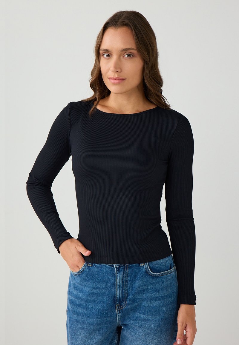 Schwarzes, geripptes Langarmshirt mit rundem Halsausschnitt, kombiniert mit hoch taillierten blauen Jeans. Enganliegendes Design und glatte Textur.