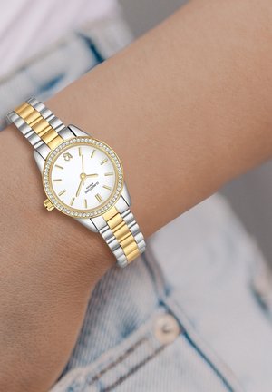 Montre-bracelet en argent et or avec un cadran rond blanc, un cadran incrusté de cristaux et un bracelet en métal à maillons alternant les couleurs.