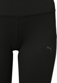 Leggings noirs en matière extensible, avec une taille haute et un petit logo gris foncé sur la partie inférieure de la jambe droite.