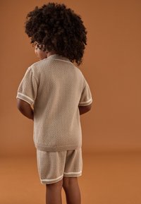 Strickoberteil mit kurzen Ärmeln und Shorts in Beige, mit strukturiertem Muster, geripptem Kragen und Bündchen sowie weißen Akzenten am Saum und an den Ärmeln.
